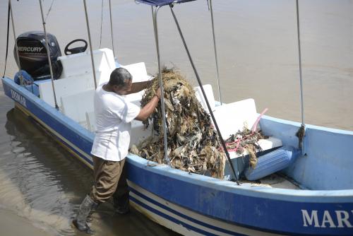 Uno de los pobladores de El Quetzalito retira de la lancha los desechos plásticos que se enredaron en la biobarda artesanal. (Foto: Wilder López/Soy502)