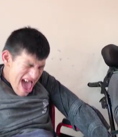 Este menor con gestos manifiesta su molestia al tener amarrados sus brazos a la silla de ruedas. (Foto: Disability Rights International)
