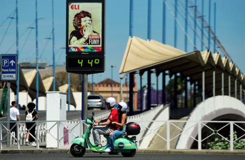 Una pareja conduce una motocicleta frente a un termómetro callejero que marca los 44 grados centígrados en Sevilla. (Foto: AFP)