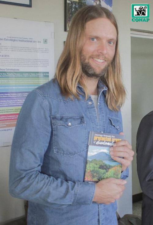 El guitarrista de Maroon 5, James Valentine, muestra un libro sobre las áreas protegidas en Guatemala. (Foto Conap)