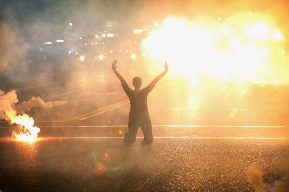 Gas lacrimógeno se observa y una mujer arrodillada en la calle con las manos al aire, después de una manifestación por el asesinato de un adolescente en Ferguson, Missouri. (Foto: AFP)&nbsp;