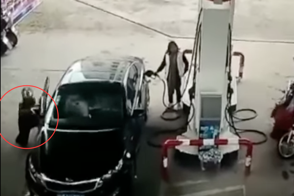 Momento en que el ladrón extrae el bolso del vehículo de la mujer que llena despreocupada el tanque de combustible. (Imagen: captura de pantalla)