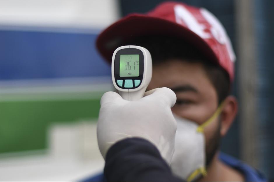 Un agente municipal de Villa Nueva toma la temperatura a un peatón, como parte de las medidas para evitar la propagación del Covid-19. (Foto: AFP)