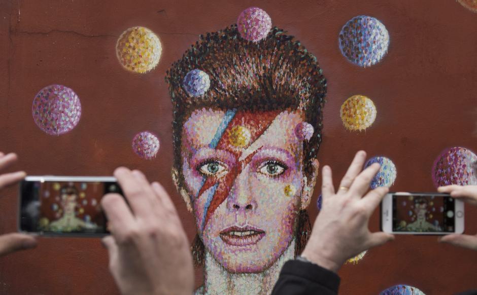 Dos fans hacen fotos de un mural del cantante británico David Bowie en Brixton, Londres (Reino Unido). El legendario músico británico David Bowie, autor de clásicos como "Starman" y "Space Oddity", ha muerto a los 69 años de cáncer, informa hoy su página de Facebook. (Foto: EFE/Will Oliver)