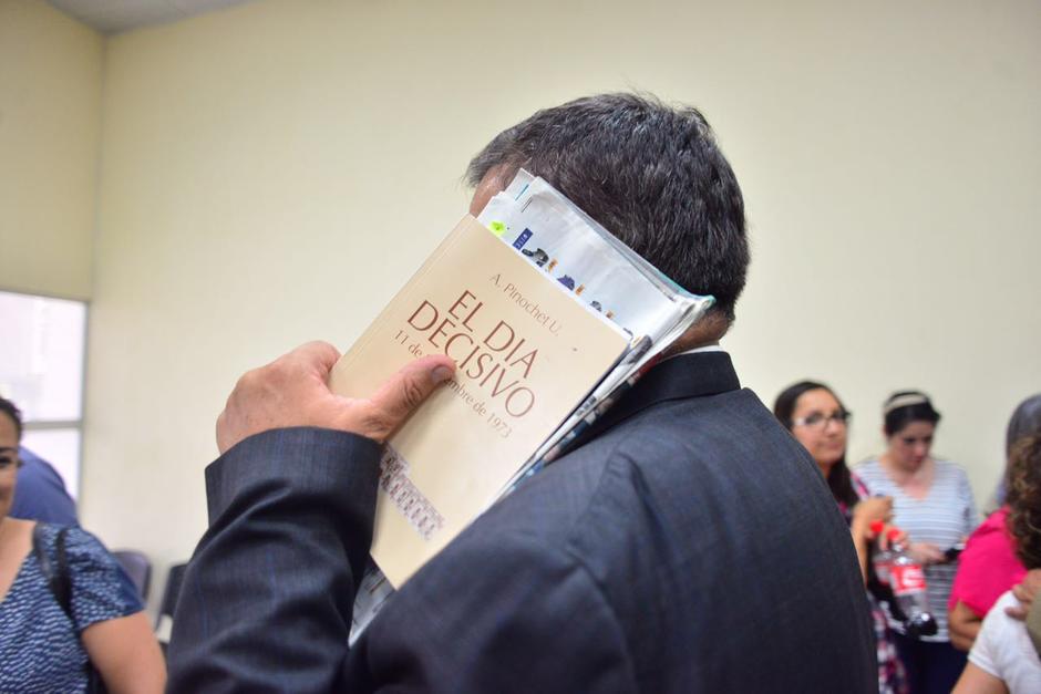 El exdiputado Carlos Herrera se cubre el rostro al salir de una diligencia judicial con el libro "El Día Decisivo" de Augusto Pinochet. (Foto: Jesús Alfonso/Soy502)&nbsp;
